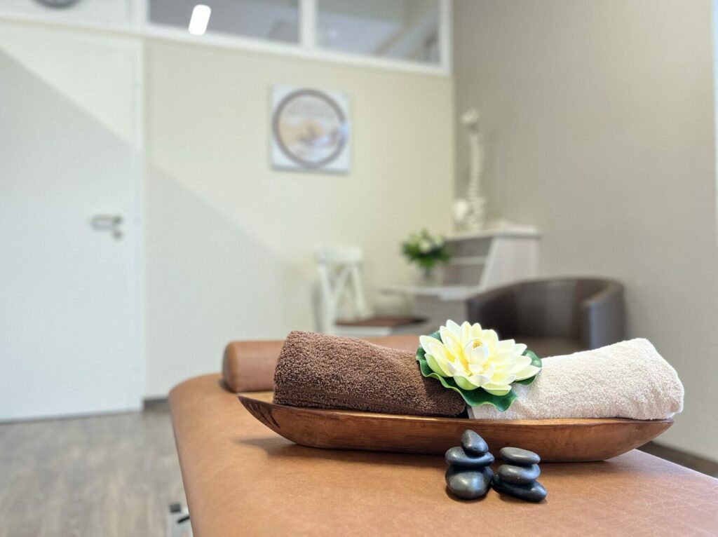 Behandlungsraum mit Therapieliege und dekorativen Wellness Handtüchern und Steinen im Therapiezentrum Am Kapellchen in Kerpen-Balkhausen